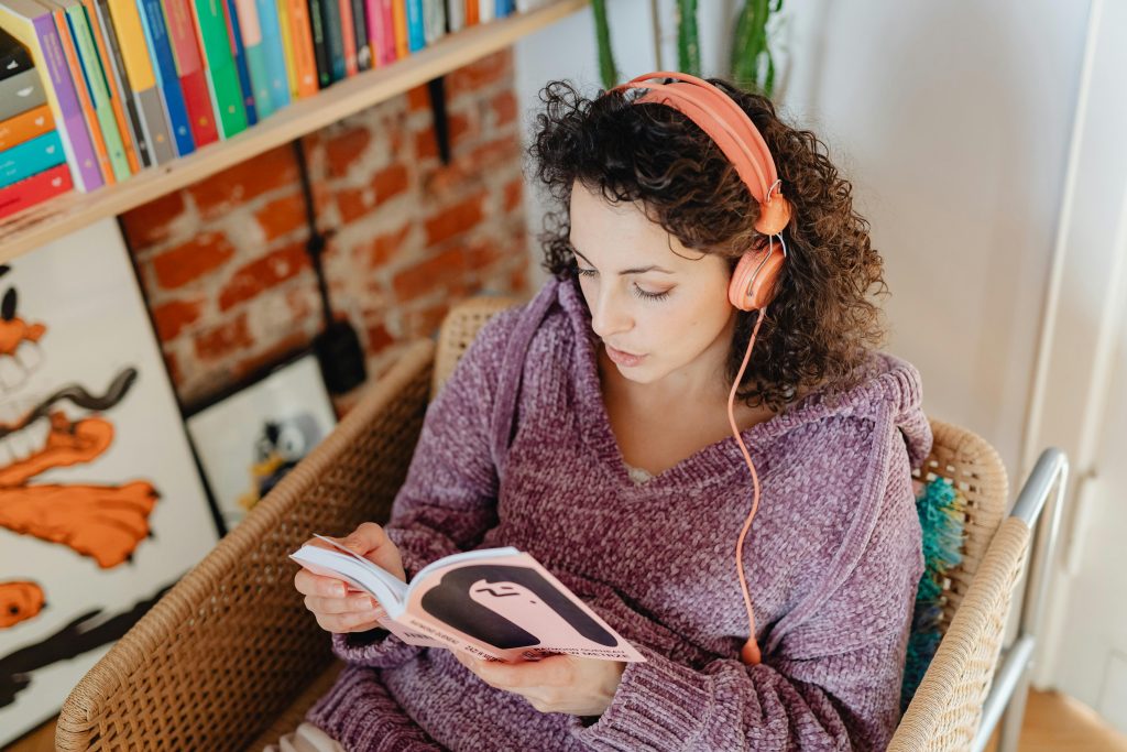 Photo by Photo By: Kaboompics.com: https://www.pexels.com/photo/woman-with-headphones-reading-a-book-at-home-6633276/